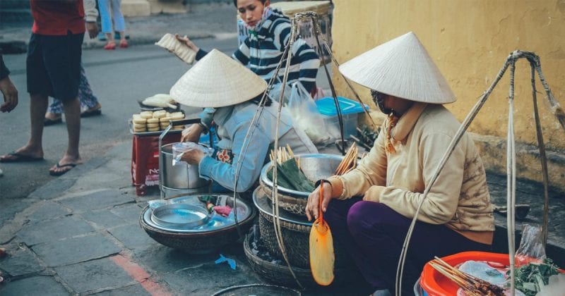 A vietnamese street hawker fanning meat skewers