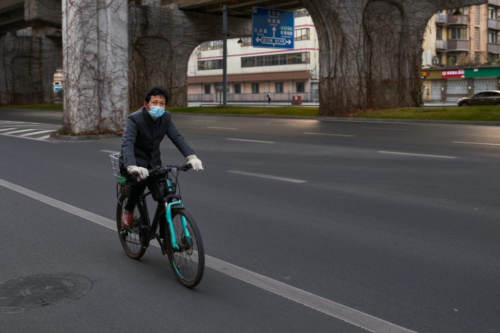 A man with face mask riding a bicycle on an empty road during China's lockdown