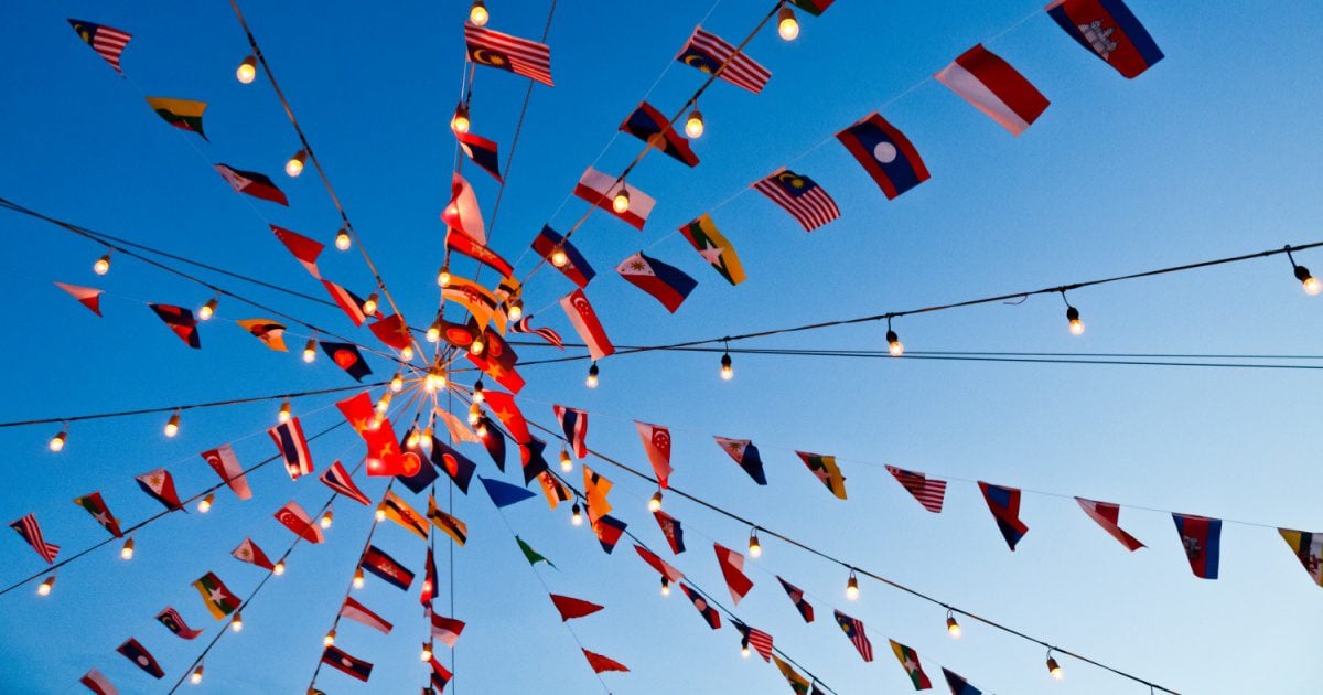 A photo showing the perspective of someone looking up at a conical structure made of many buntings that have various flags of ASEAN countries on them. A clear blue sky forms the background.